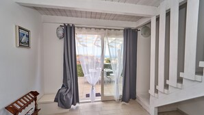 Une pièce dotée d’une porte-fenêtre coulissante donnant sur un espace extérieur, d’un banc en bois et d’une petite étagère ornée d’objets décoratifs.