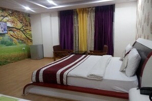 A hotel room with a bed, a desk, a chair, and a TV mounted on the wall. - Hotel Green View palace (Noida)