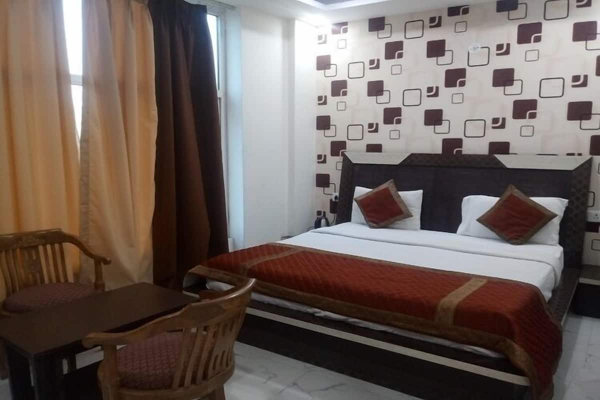 A hotel room with a bed, a wooden chair, a small table, and a patterned wall.