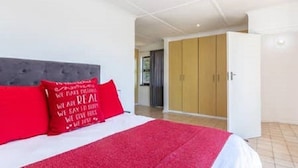 A bedroom with a bed, a red throw, a wardrobe, and a door leading to another room.