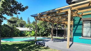 A covered patio area with a pool, surrounded by a well-maintained lawn and trees.