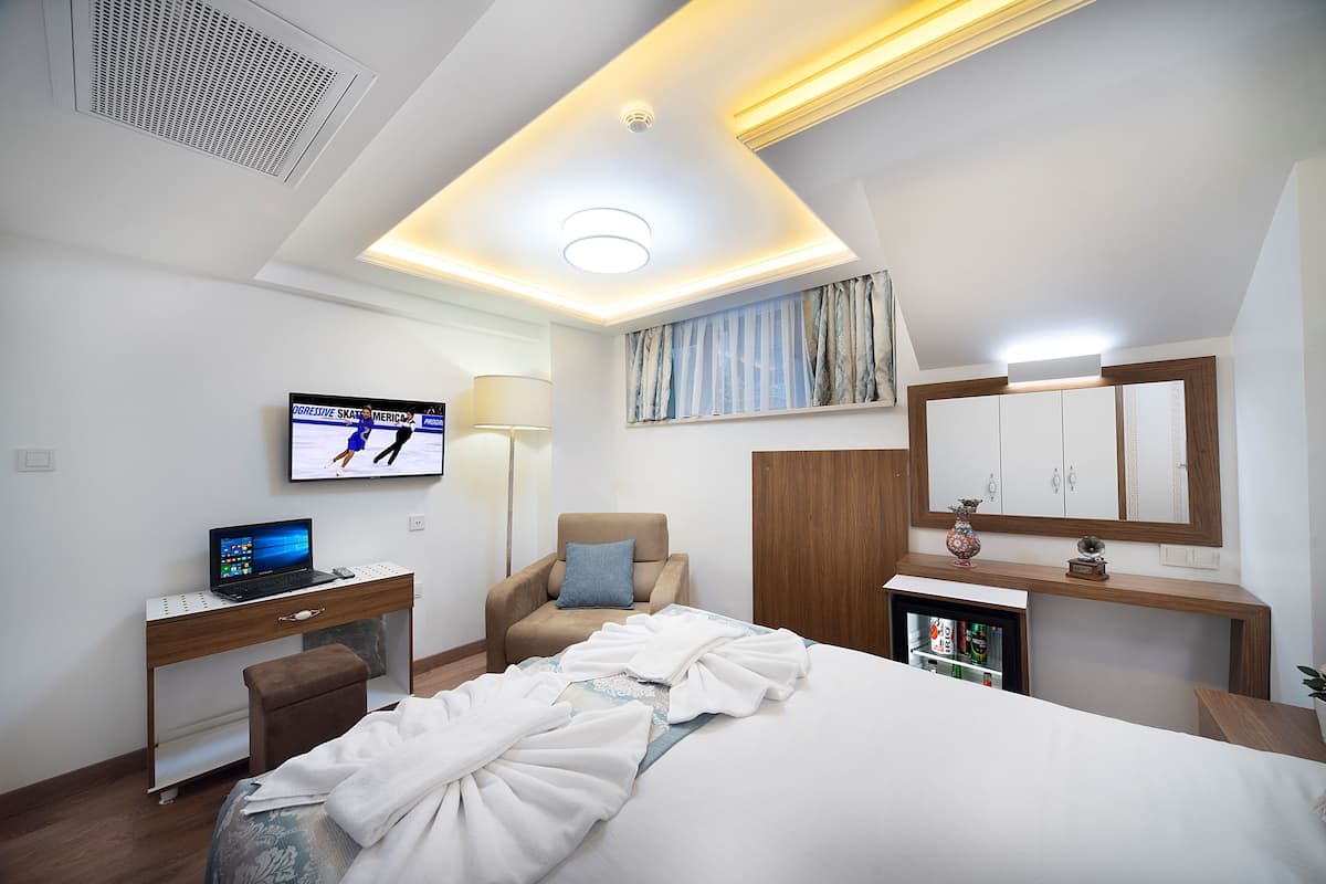 A hotel room with a bed, desk, chair, TV, and a small cabinet.