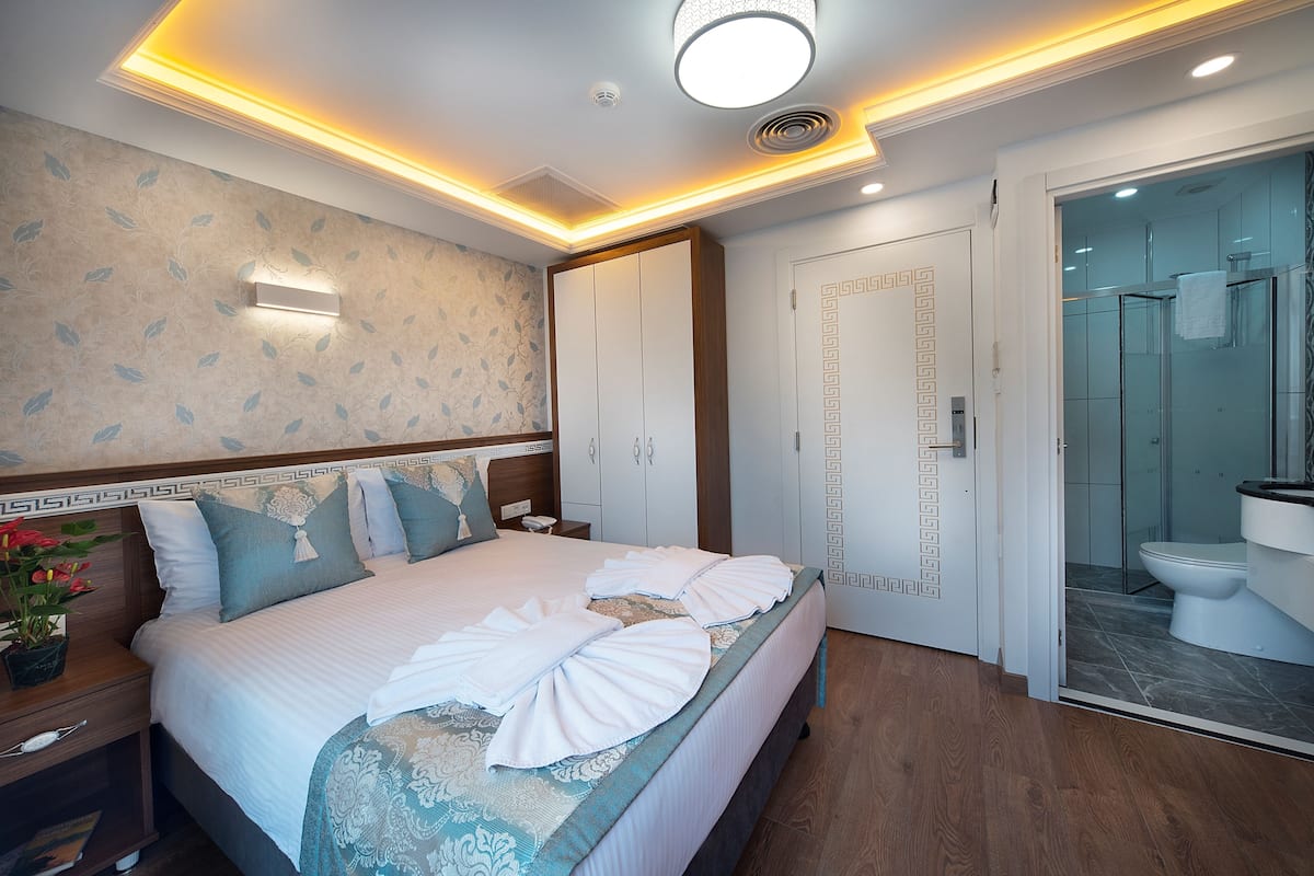 A hotel room with a large bed, a wardrobe, a bathroom with a glass shower, and a decorative wall.