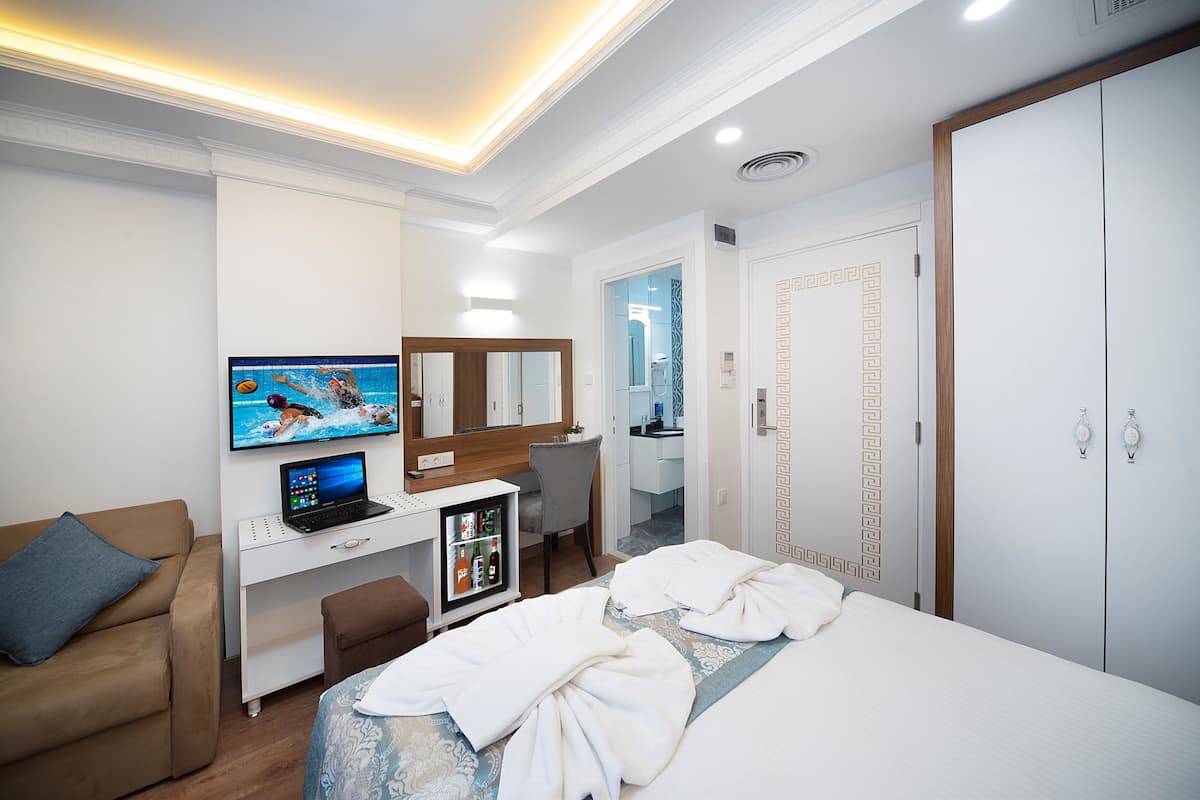 A hotel room with a bed, a desk with a laptop, a TV, a chair, and a wardrobe.