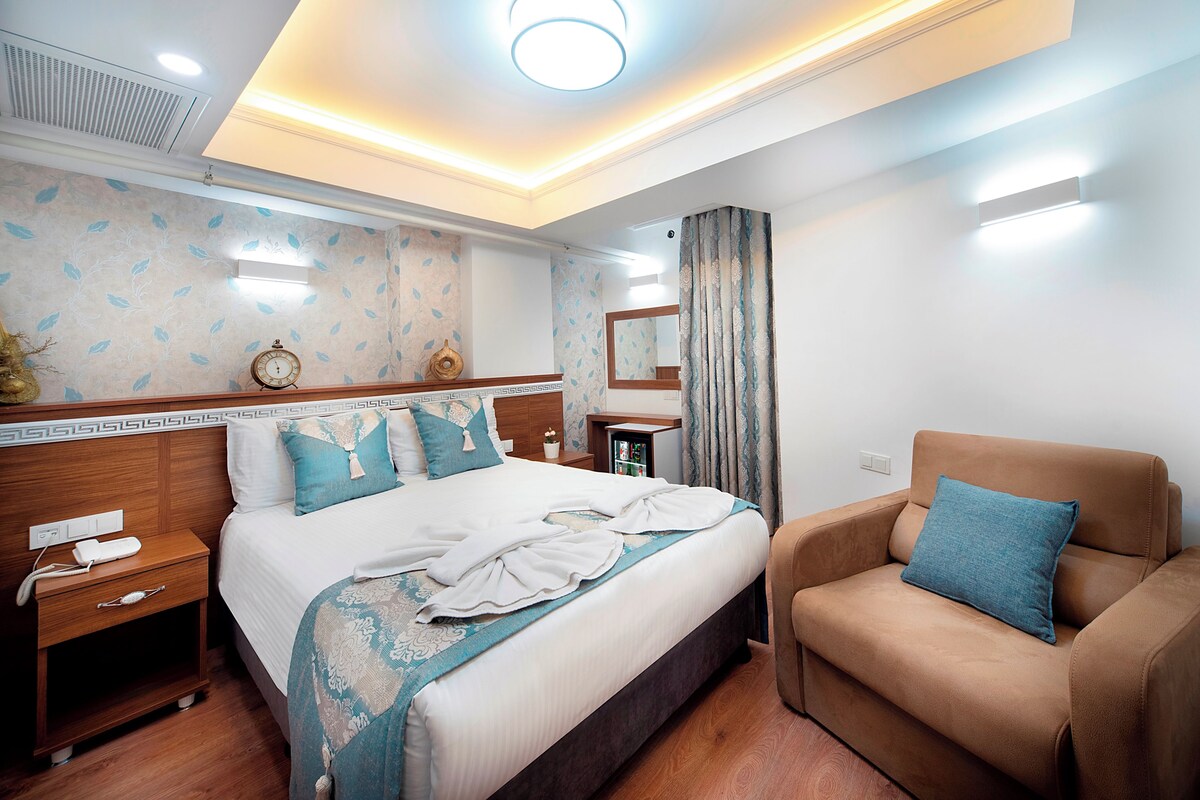 A hotel room with a bed, bedside table, nightstand, and a sofa.