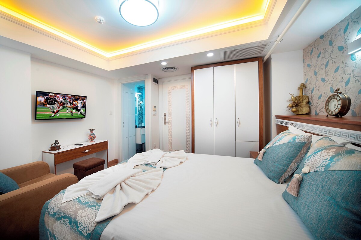A bedroom with a bed, a TV, a desk, a wardrobe, and a nightstand.