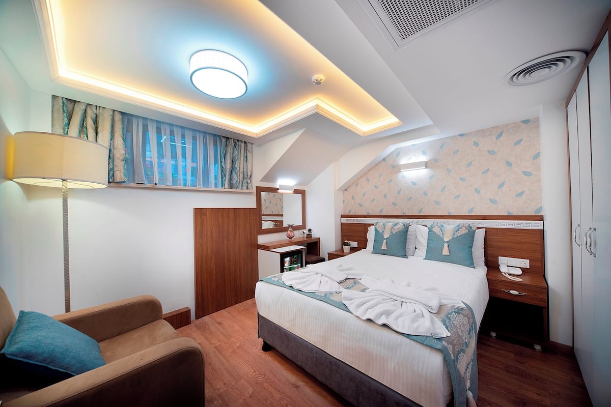A hotel room with a bed, a desk, a chair, a lamp, and a wardrobe.