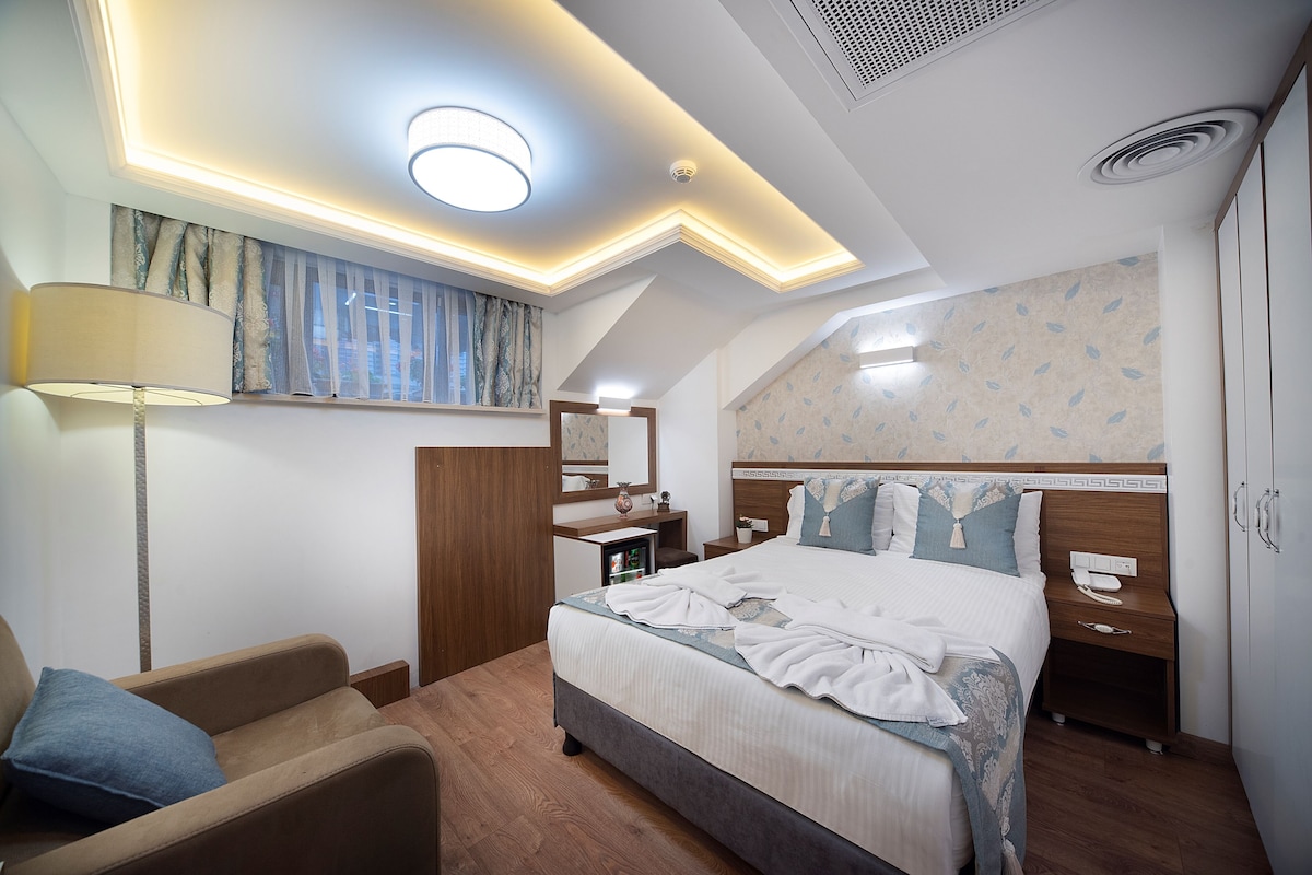 A hotel room with a neatly made bed, a bedside table with a lamp, a wardrobe, and a ceiling with recessed lighting.