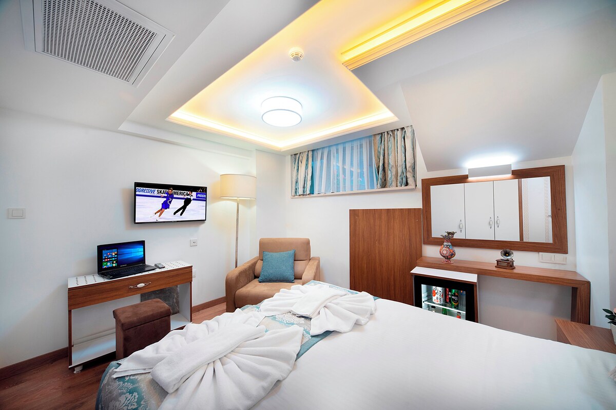 Una habitación de hotel con cama, escritorio, silla, televisor y un armario pequeño.