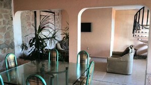A dining area with a glass table and plaid chairs, a stone wall, and a staircase leading to another level. - Teques Vacation Home, Golden Zone "Las Alas" Lake View (Tequesquitengo)