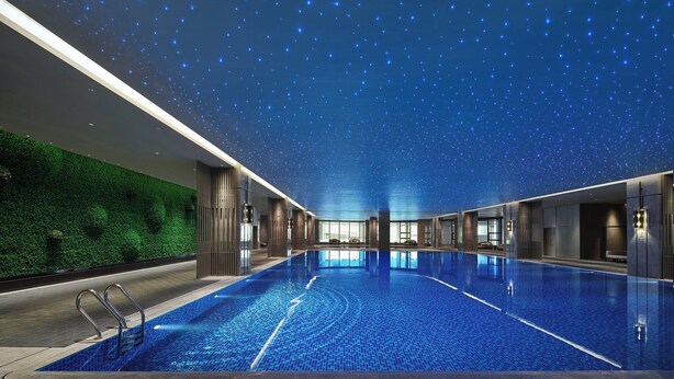 Une vaste piscine intérieure dotée d’un plafond étoilé, entourée d’une architecture moderne et d’un mur végétal.