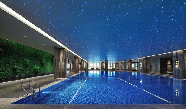 Une vaste piscine intérieure dotée d’un plafond étoilé, entourée d’une architecture moderne et d’un mur végétal.