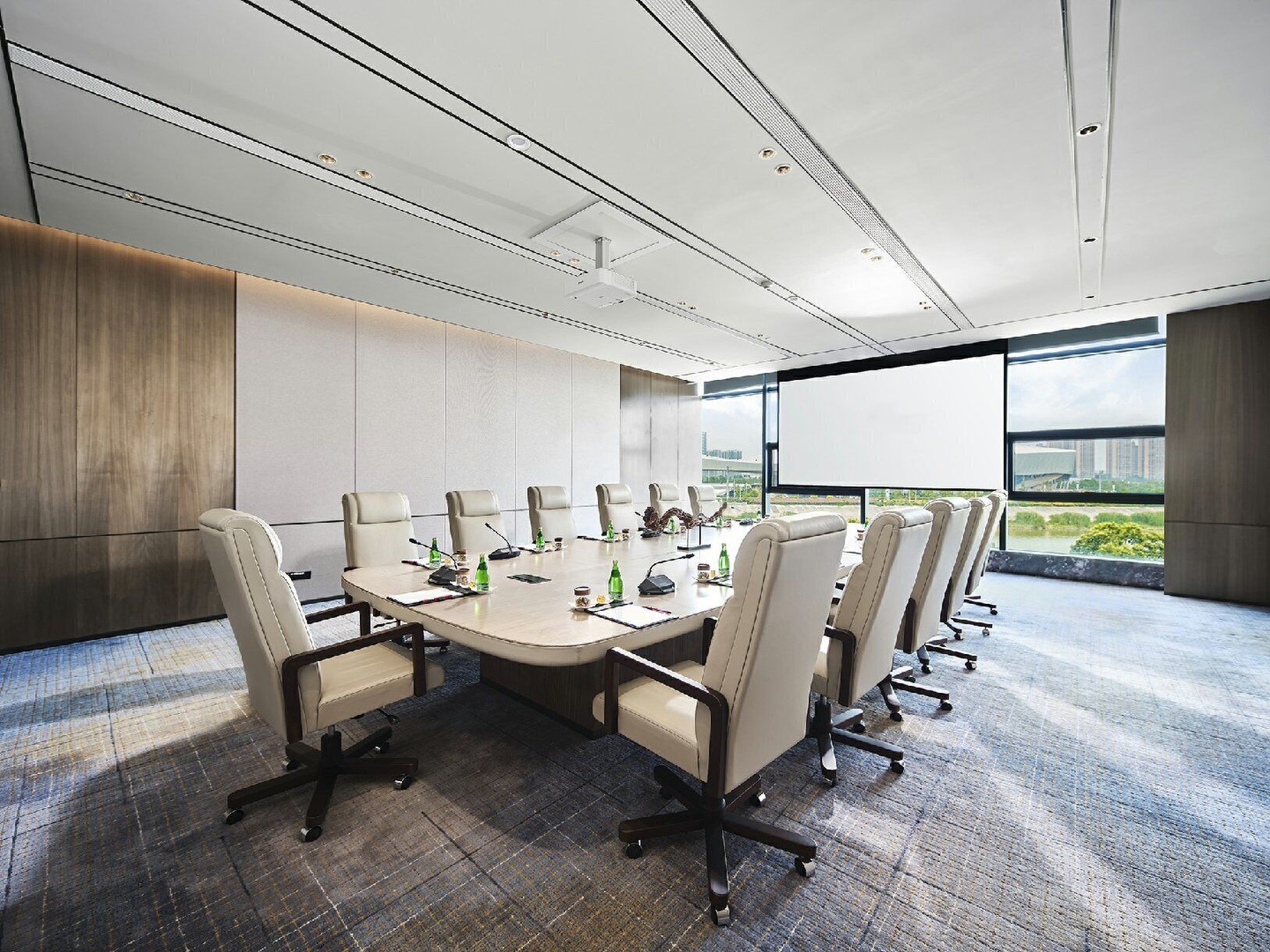 A conference room with a large table, multiple chairs, and a view of a cityscape through large windows.