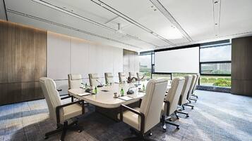 A conference room with a large table, multiple chairs, and a view of a cityscape through large windows.