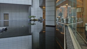 Een modern interieur met een reflecterend waterobject, een zithoek met banken en een glazen scheidingswand.