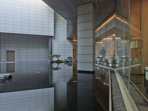 Un intérieur moderne agrémenté d’un élément décoratif aquatique réfléchissant, d’un espace salon avec des canapés et d’une cloison en verre.