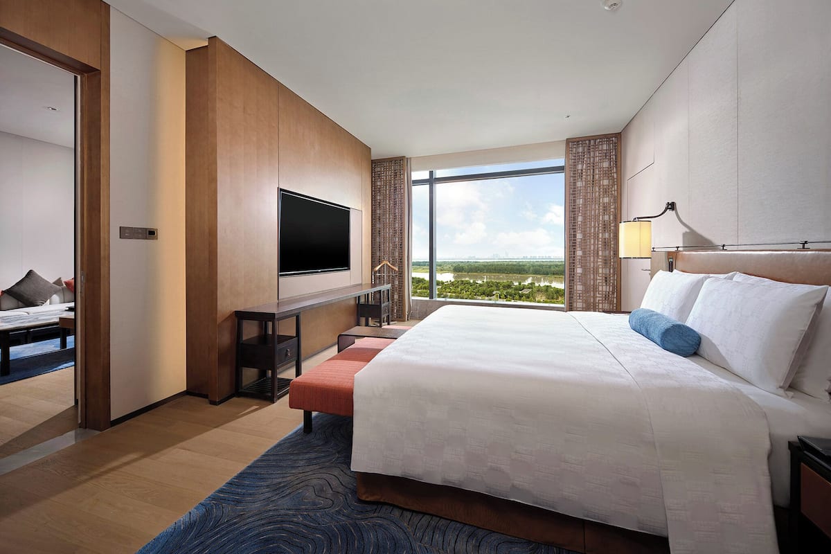 Una habitación de hotel moderna con una cama grande, un televisor de pantalla plana montado en la pared, un escritorio con una silla y un ventanal con vistas a la ciudad.