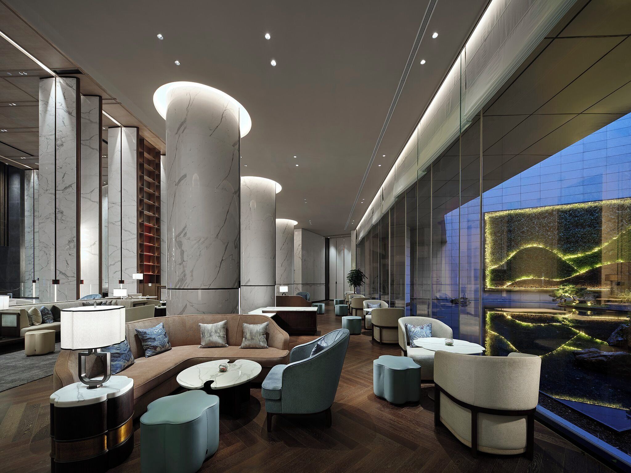 A modern lobby with marble columns, seating areas, and a large window with a view of a landscaped area.