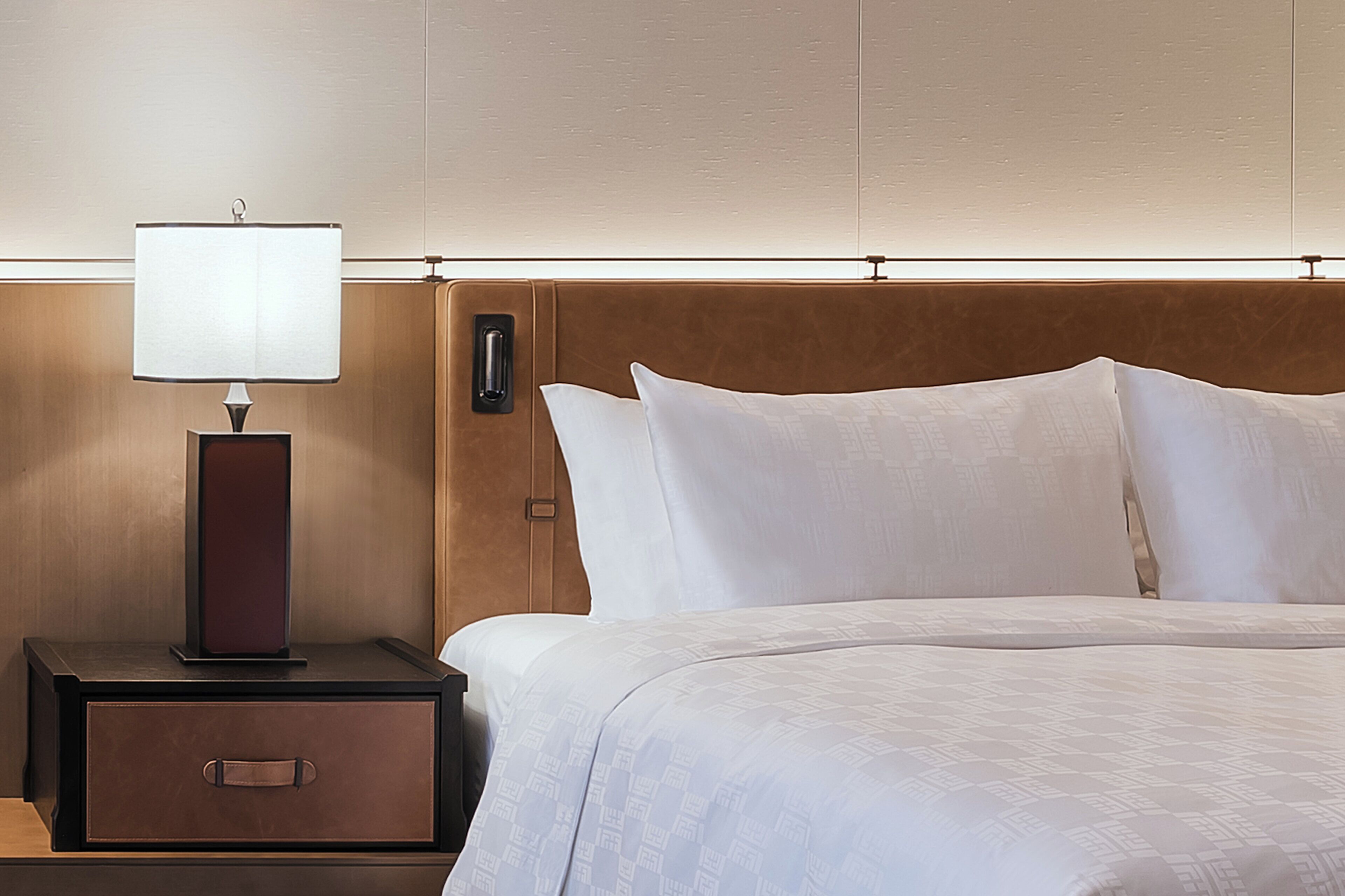 Una habitación de hotel con una cama, una mesita de noche con lámpara y un cabecero de madera.