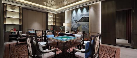 A spacious room with a large, round table surrounded by chairs, a bookshelf, and a painting on the wall.
