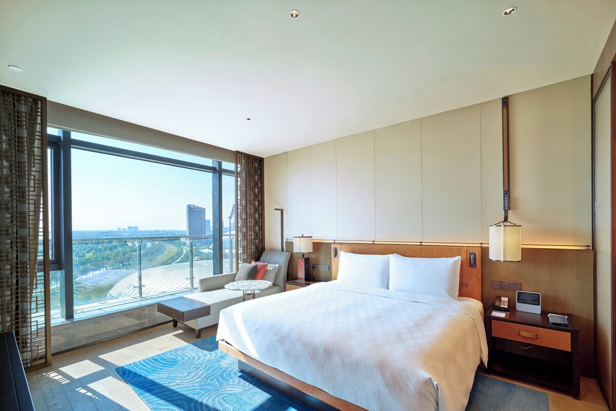 Une chambre d’hôtel moderne dotée d’un grand lit, d’un coin salon et offrant une vue sur le paysage urbain.