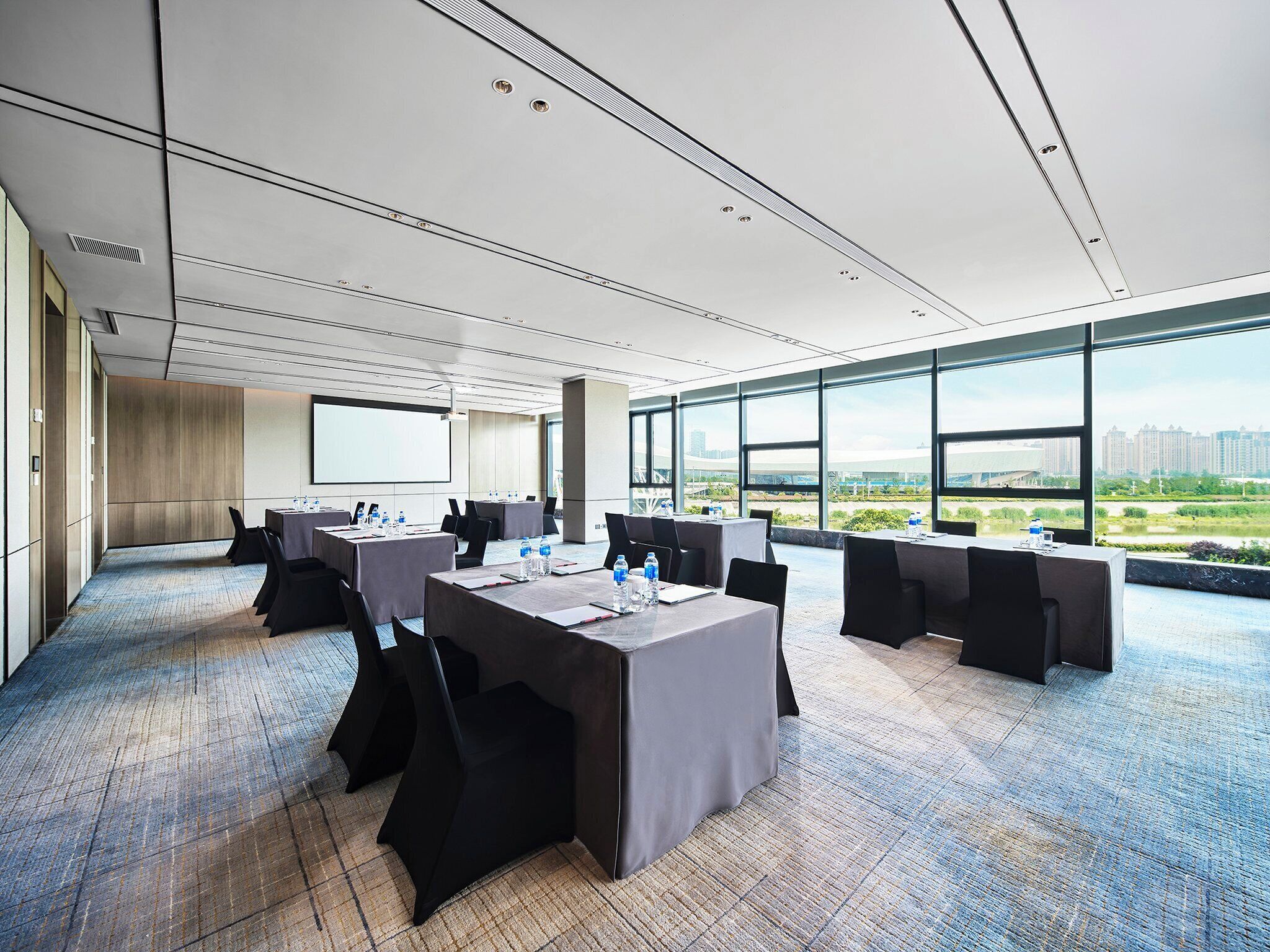 A conference room with multiple tables, chairs, and a large screen.