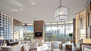 Een ruime lobby met moderne inrichting, een groot televisiescherm en uitzicht op de stad door brede ramen.