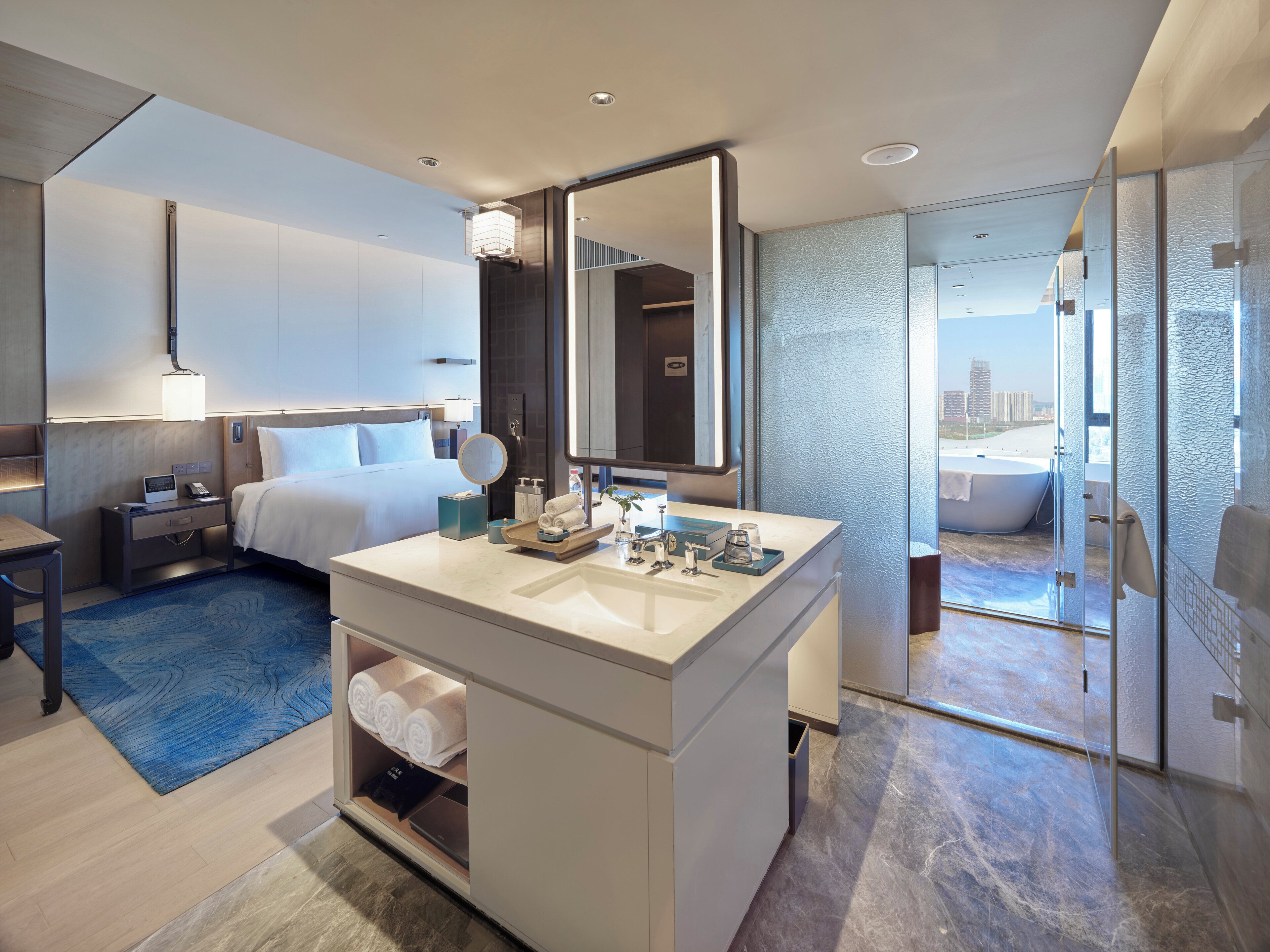 Habitación de hotel moderna con una cama grande, un tocador con espejo, una bañera y vistas a la ciudad.