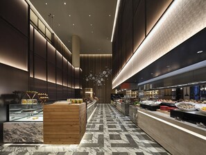Un hall d’hôtel moderne avec un comptoir d’accueil central, un sol carrelé en marbre et un luminaire fixé au mur.