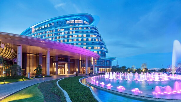 A modern hotel with a curved facade, a fountain in the courtyard, and a well-lit entrance. - HUALUXE Nanjing Yangtze River by IHG (Nanjing)