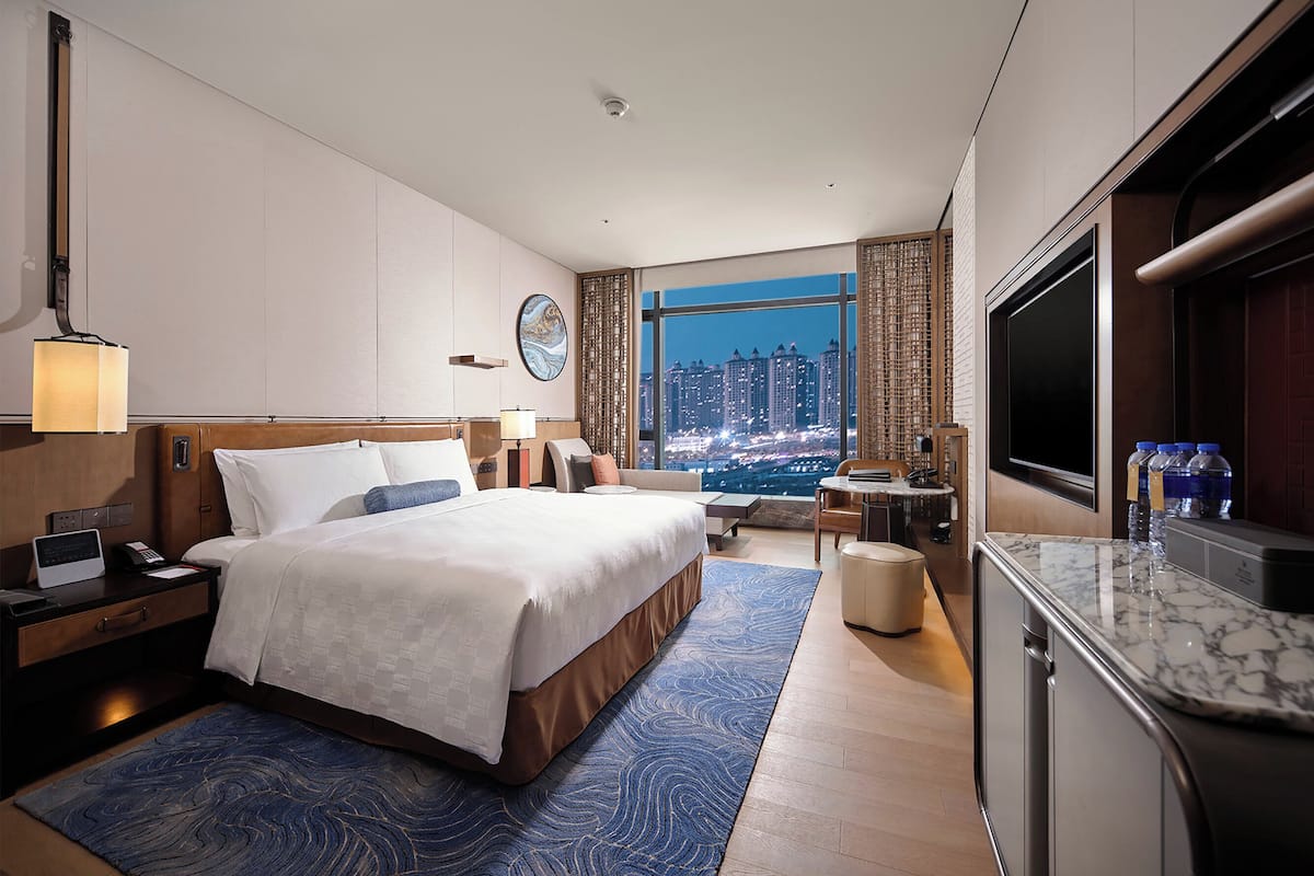 Habitación de hotel moderna con una cama grande, un escritorio, un televisor y vistas a la ciudad.