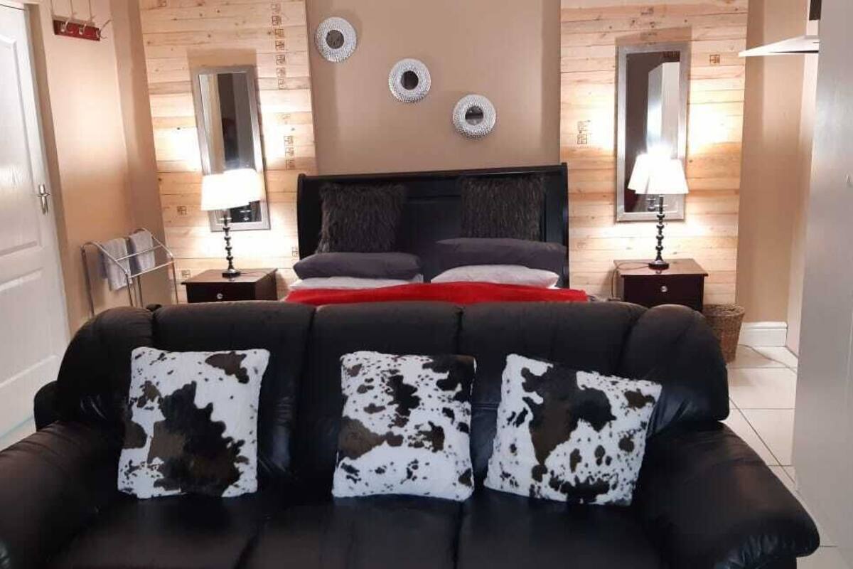 A bedroom with a black leather sofa, a bed with a dark headboard, and two bedside tables with lamps.