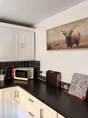 Een keuken met witte kastjes, een magnetron, een broodrooster en een schilderij van een jak.