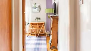 Un passadís que condueix a una habitació amb terra de fusta, una catifa morada, una taula i una làmpada.