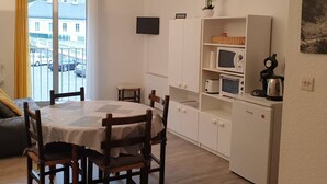 A compact living space with a dining table, chairs, a sofa, a TV, a microwave, a kettle, and a small cabinet.