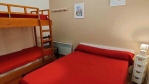 A room with two bunk beds, a radiator, a small white dresser, and two framed pictures on the wall.