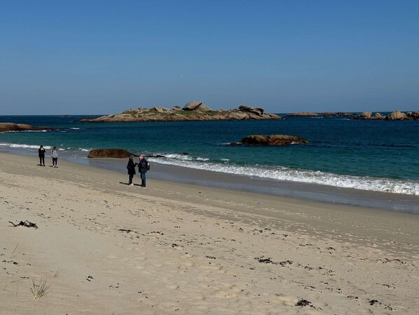 Une plage avec un ciel dégagé, des affleurements rocheux et des vagues calmes.