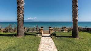 Un vialetto in pietra conduce a un cancello incorniciato da palme, con vista su un mare cristallino e blu.
