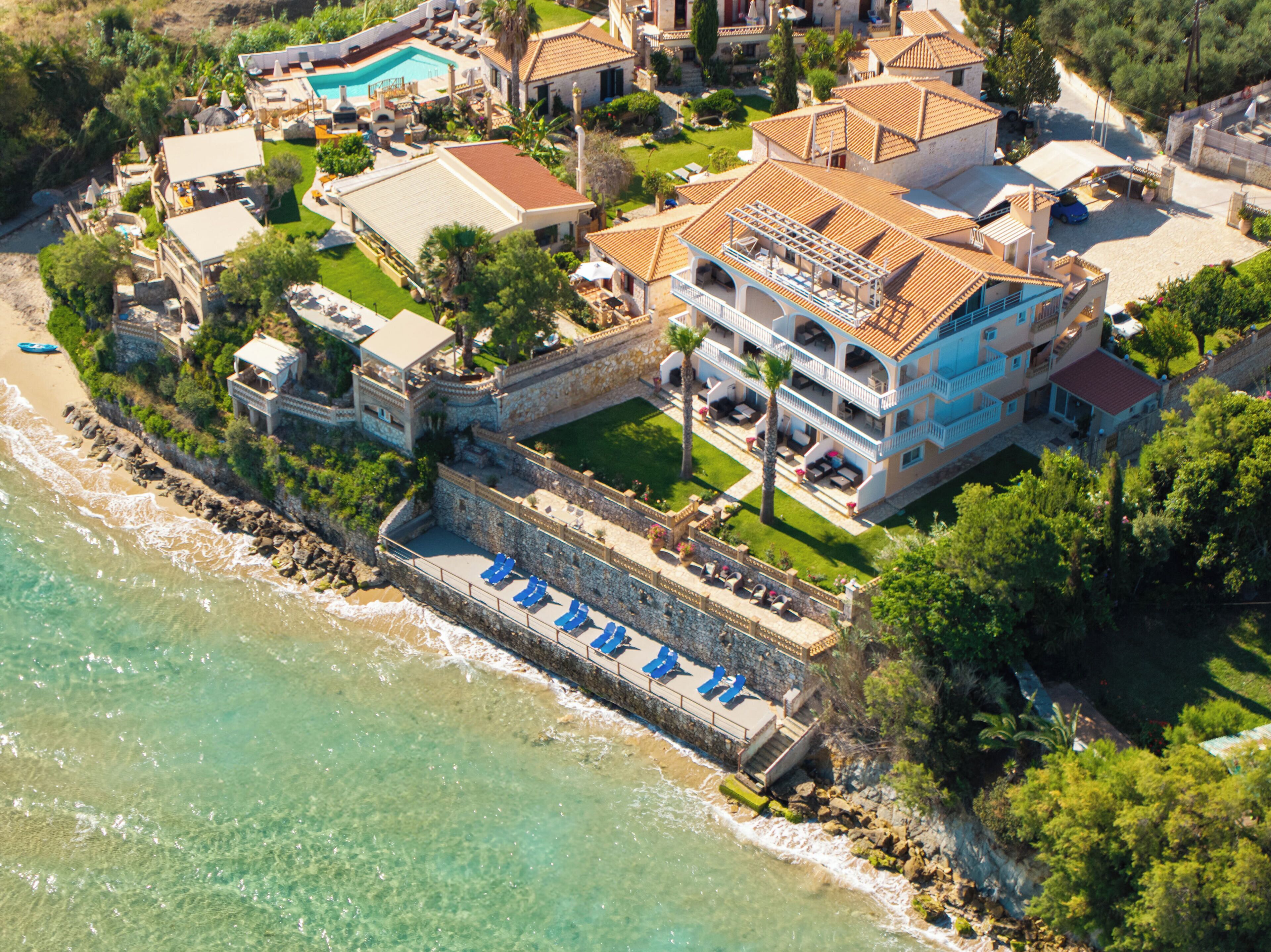 An aerial view of a coastal property with a large building, a swimming pool, and a beach area.