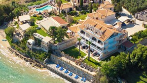 Vista aerea di una proprietà costiera con un edificio grande, una piscina e un’area spiaggia.