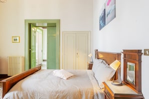 Un dormitorio con cama, lámparas de noche, un espejo y una puerta que da a otra habitación.