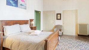 Ein Schlafzimmer mit einem hölzernen Bett, einem Nachttisch, einem Sessel, einem Heizkörper und zwei Türen.