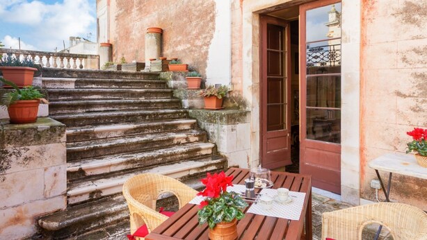 Eine Treppe führt zu einer Tür, draußen befindet sich eine Sitzgruppe mit Tisch und Stühlen, sowie Kübelpflanzen.