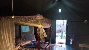 A tent-style room with a four-poster bed, a wooden bench, and a view of the outdoors.