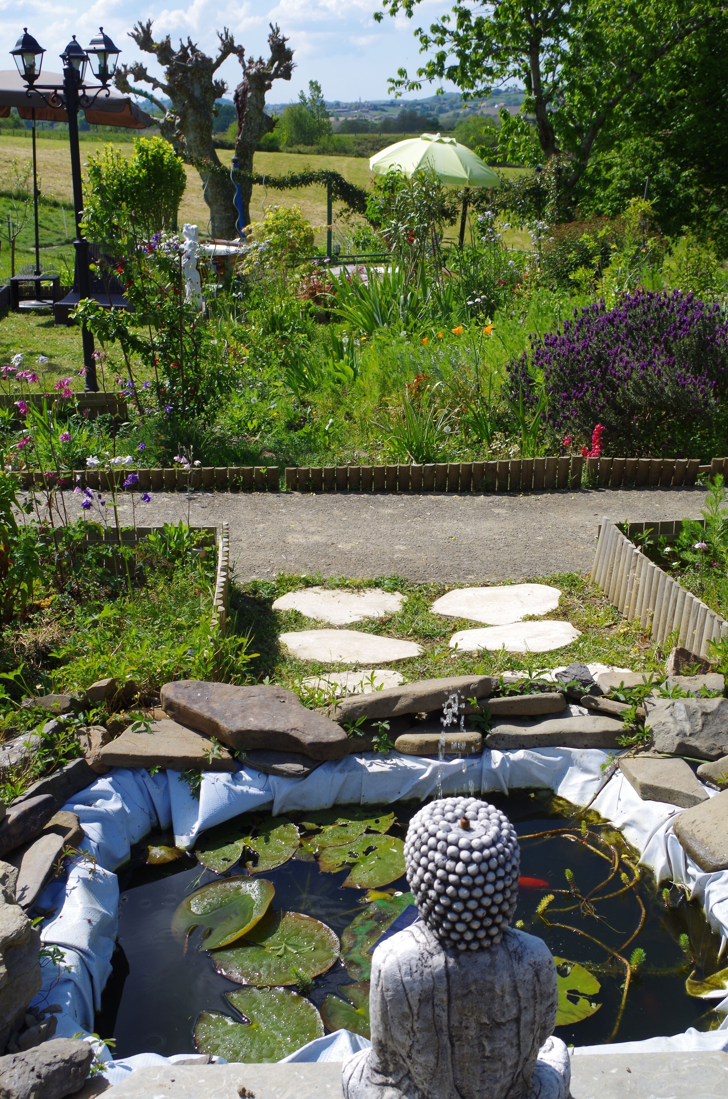 Un jardín con un estanque, piedras para pisar y una estatua de Buda.
