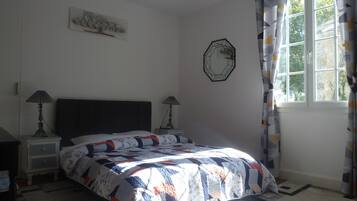 A bedroom with a bed, two bedside tables, a wall clock, and a window with curtains.