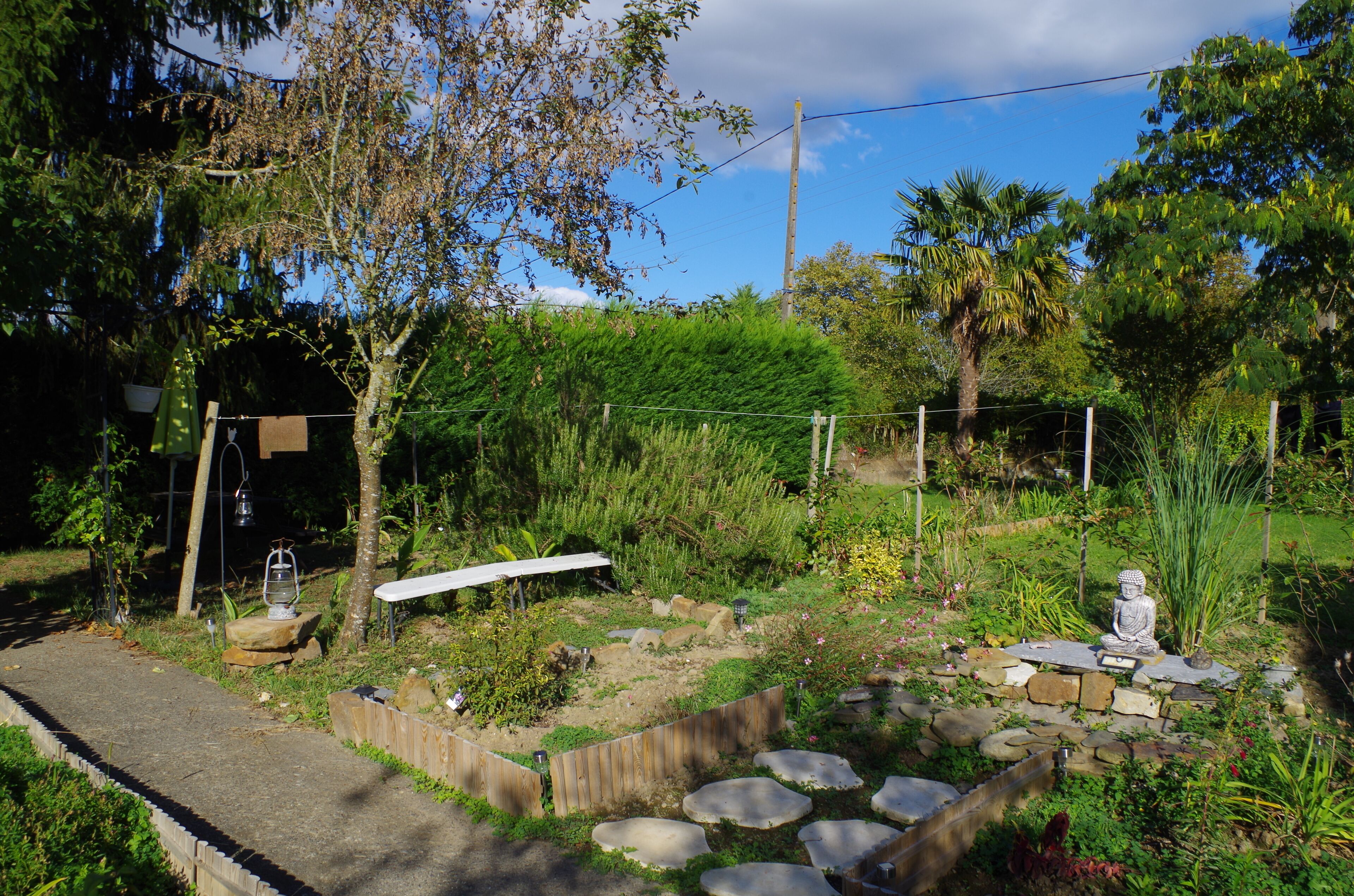 A garden with a Buddha statue, stone steps, and a wooden fence.