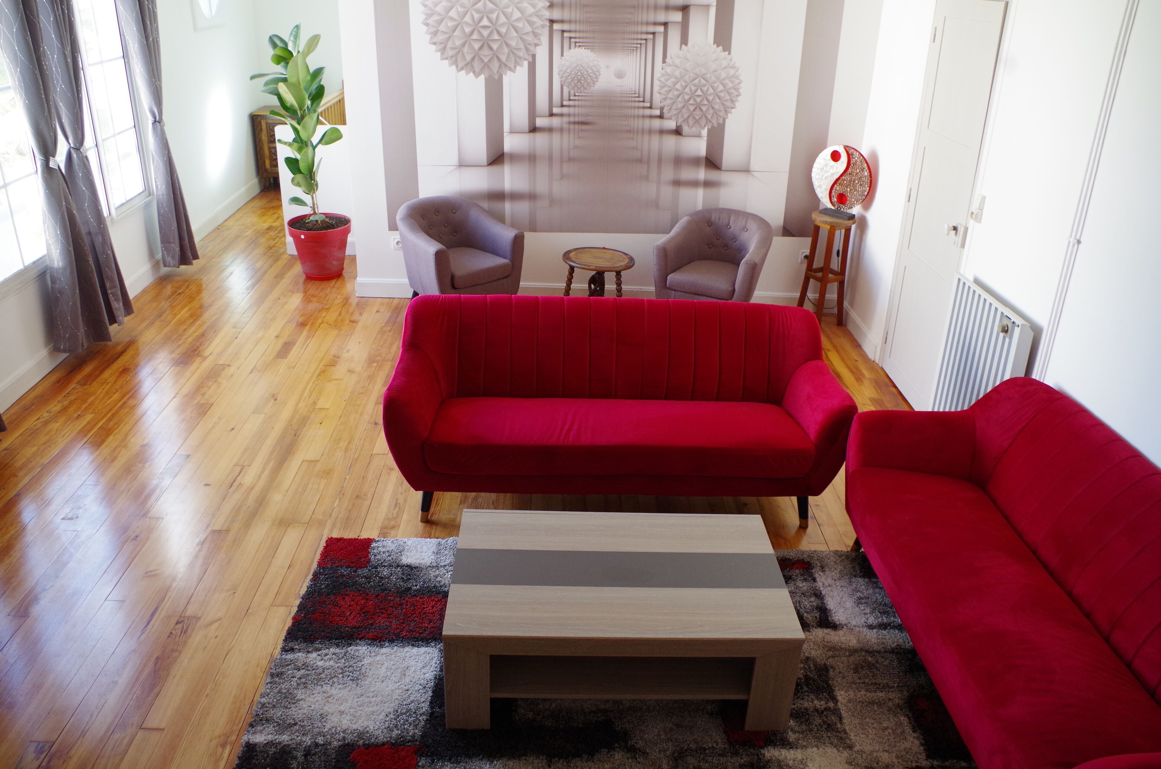 A modern living room with a red sofa, two armchairs, a small wooden coffee table, and a potted plant.