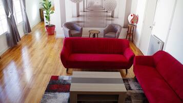 A modern living room with a red sofa, two armchairs, a small wooden coffee table, and a potted plant.