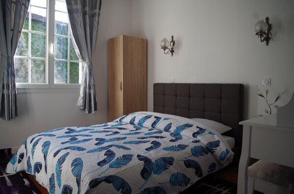 A bedroom with a bed, a wardrobe, a nightstand, and a window with curtains. - Maison Elizondoa (Masparraute)